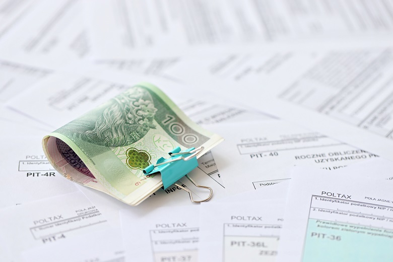 Polish zloty money PLN on big amount of polish PIT, CIT and VAT tax forms close up. Accounting, bureaucracy and taxpayers routine